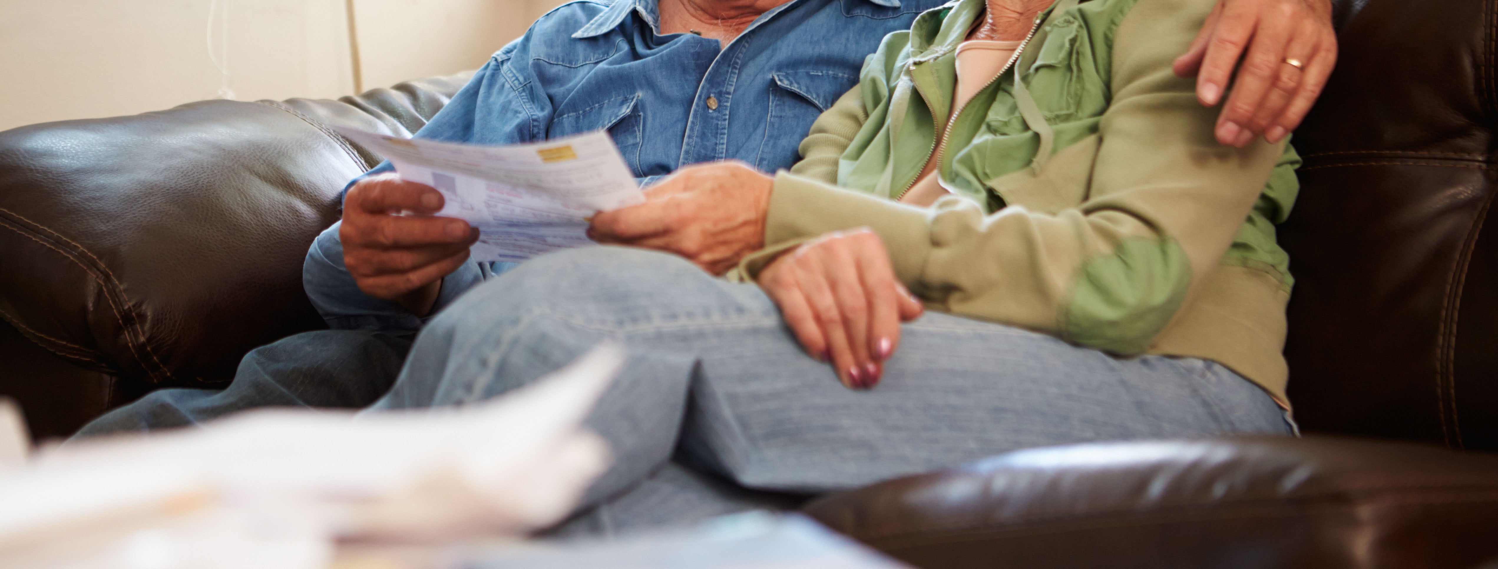 Elderly couple sitting on the couch reading bills
