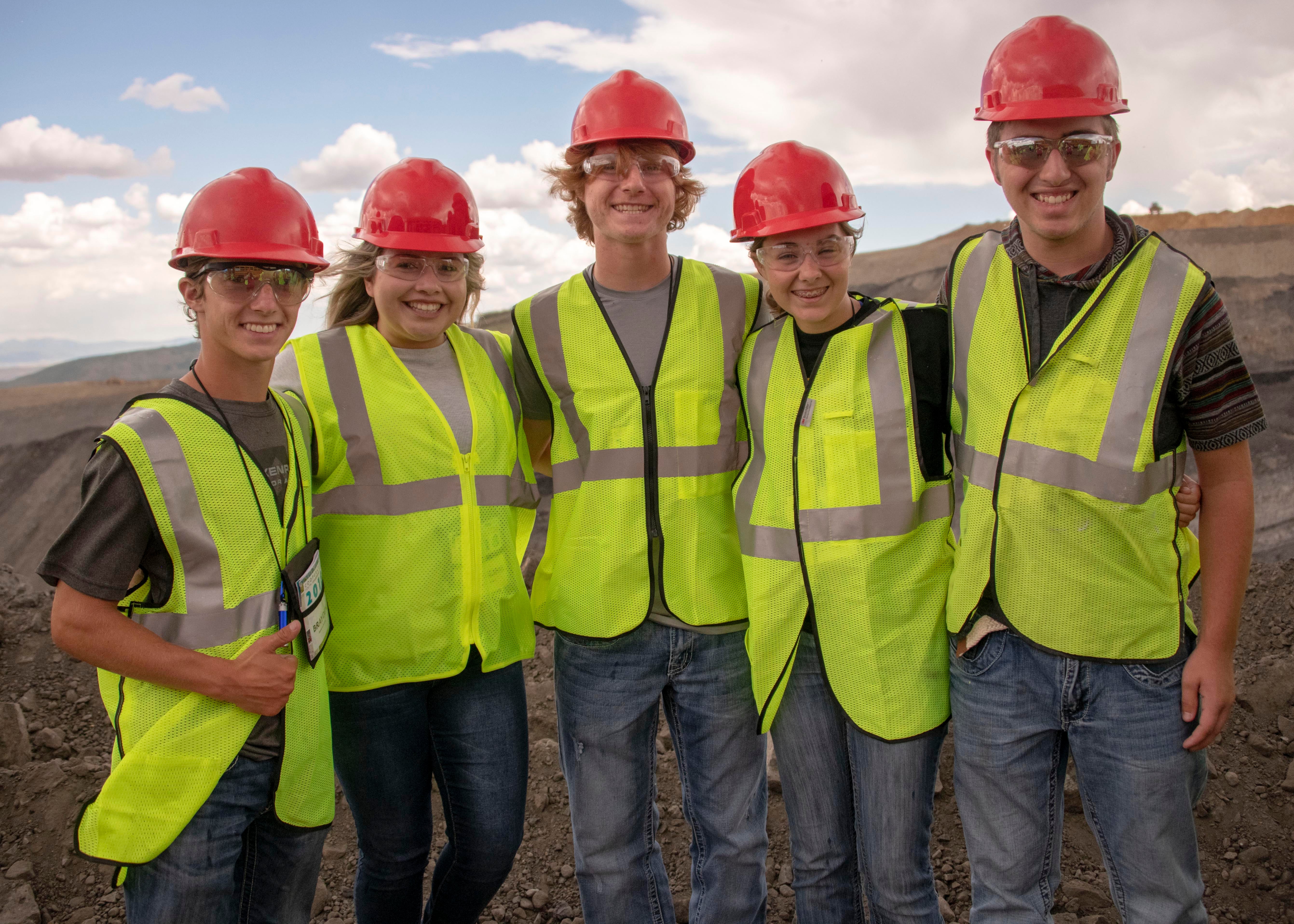 Five campers in hard hats and yellow safety vests pause for a group photo.